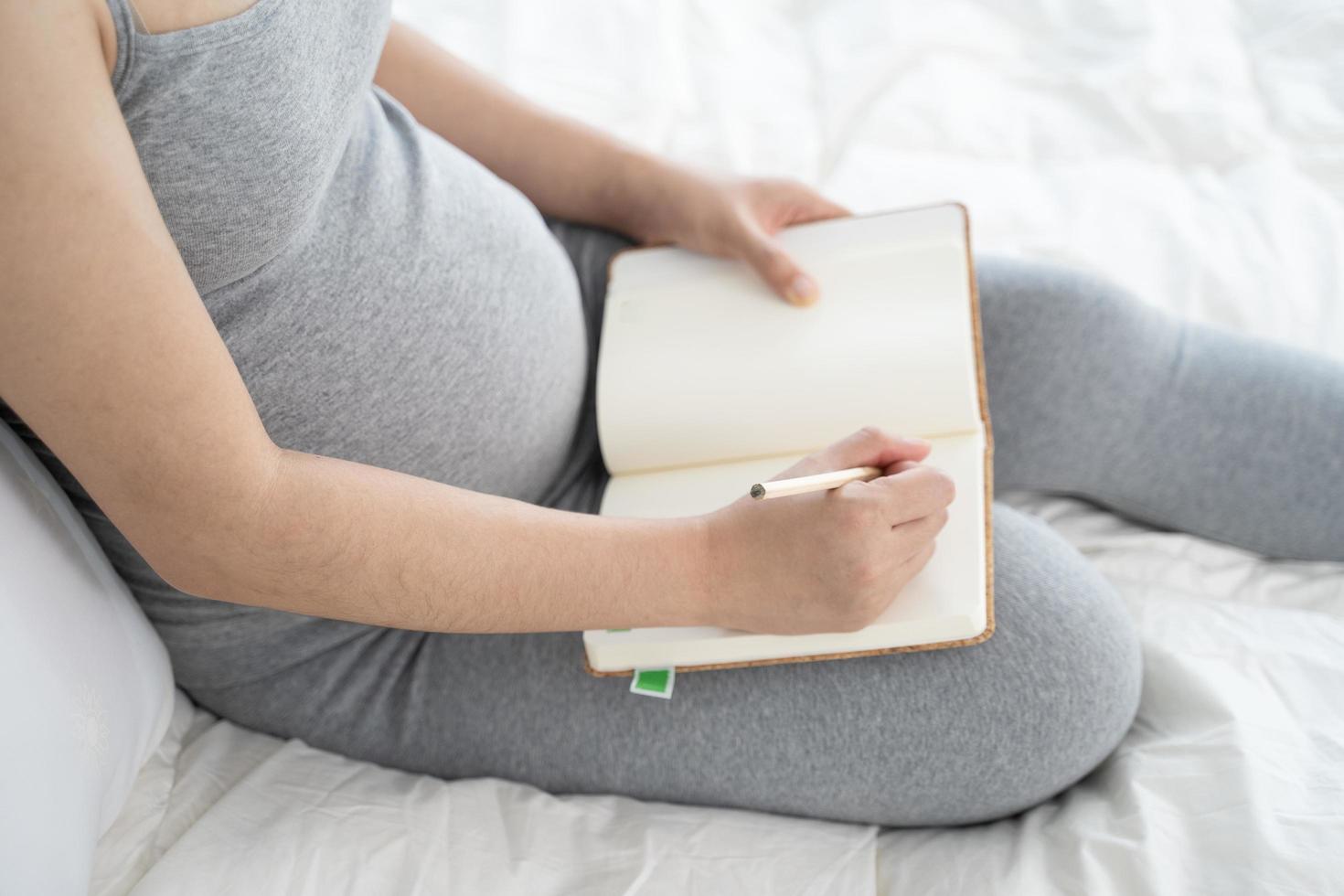 mulher grávida faz anotações no caderno. conceito de gravidez, paternidade, preparação e expectativa foto