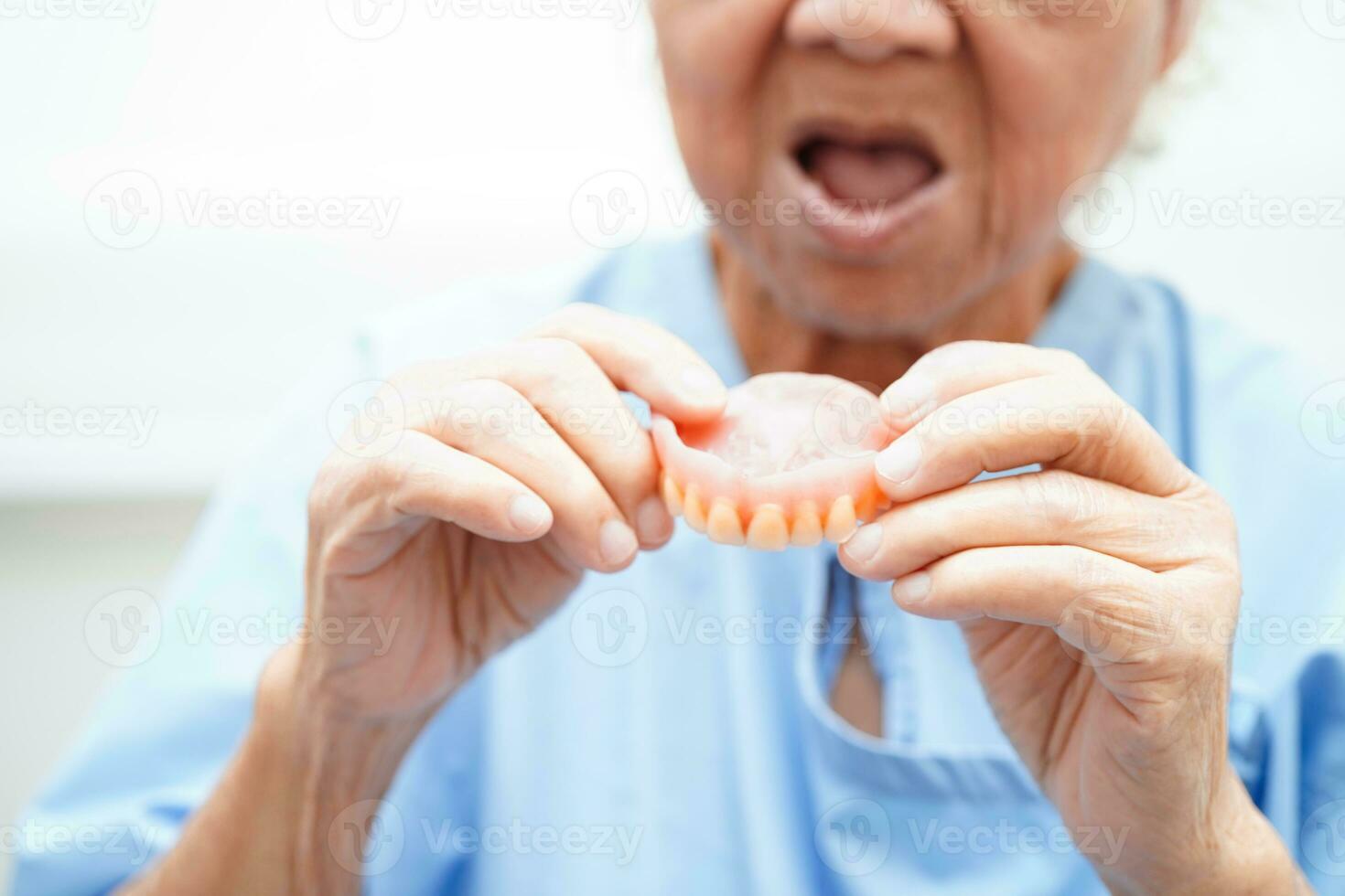 ásia Senior mulher paciente vestindo dentes dentadura para dentro dela boca para mastigar Comida. foto