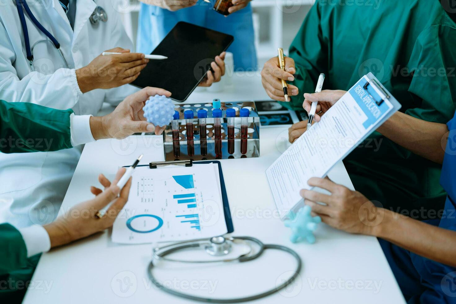 médico equipe tendo uma encontro com médicos dentro branco laboratório casacos e cirúrgico esfrega sentado às uma mesa discutindo uma pacientes trabalhando conectados usando computadores dentro a médico indústria foto
