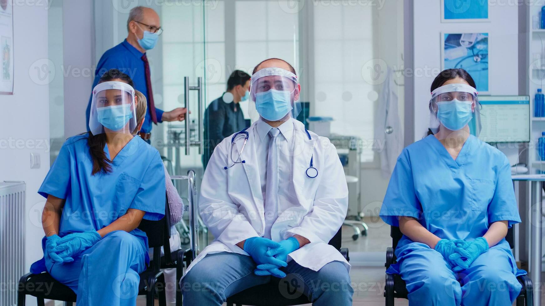 equipe do médico funcionários com proteção mascarar e viseira contra coronavírus dentro hospital esperando área olhando às Câmera. paciente dentro exame quarto para consulta. foto