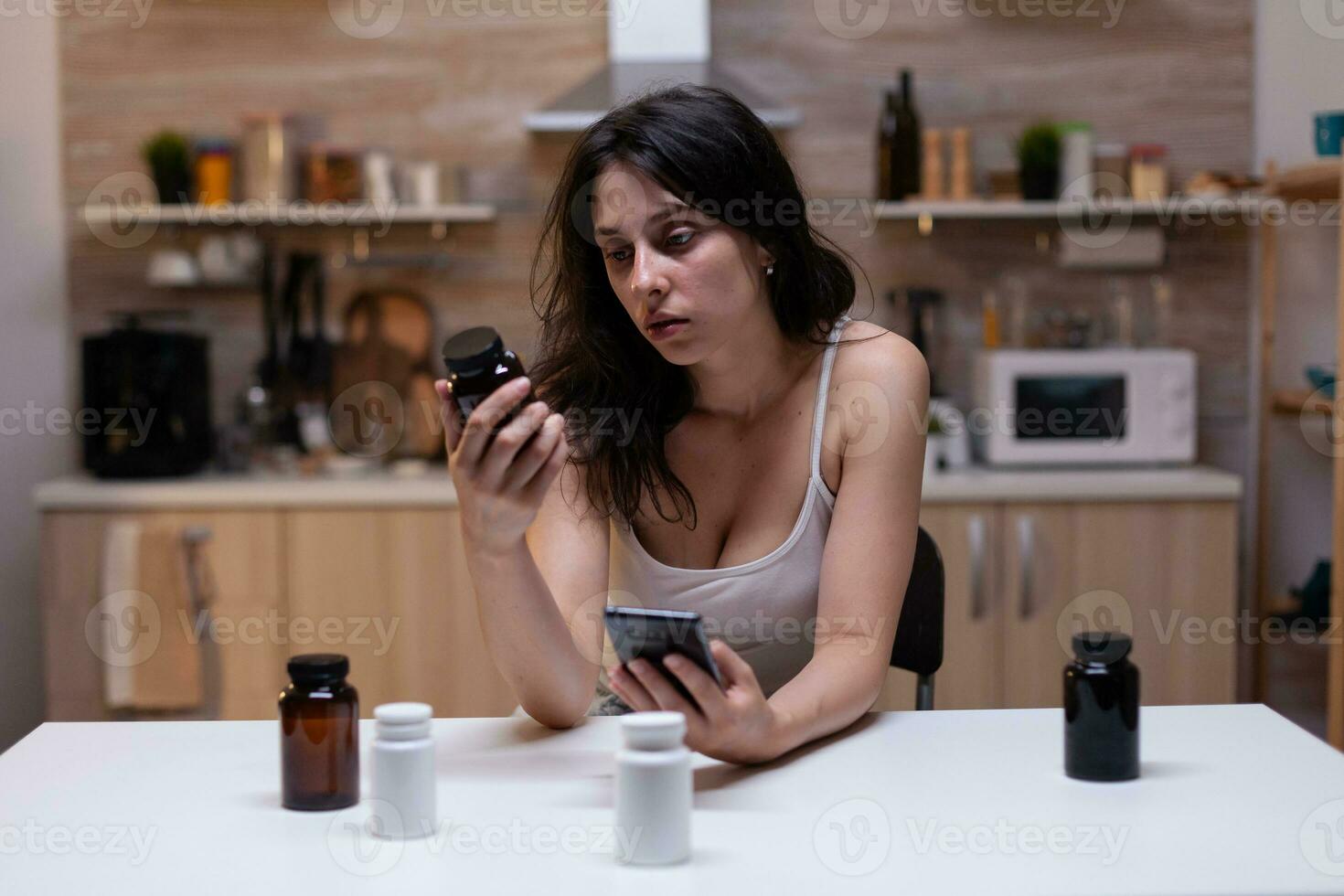 retrato do mulher com doloroso enxaqueca segurando garrafa do remédio lendo prescrição para pílulas, drogas, remédio, medicamento, tratamento e medicamento em Smartphone contra dor de cabeça foto