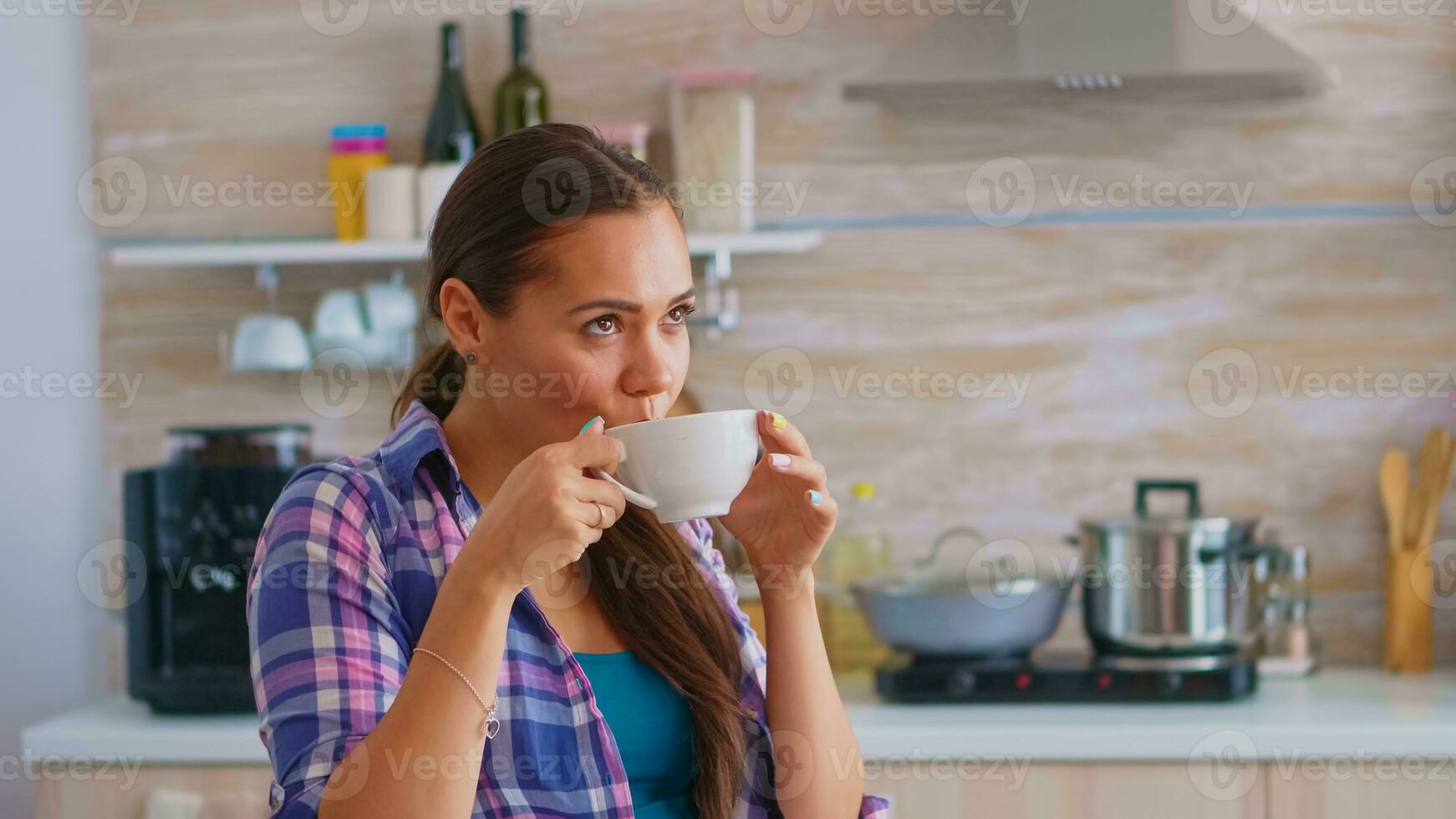 alegre sonhadores senhora bebericando quente verde chá dentro a manhã. mulher tendo uma ótimo manhã bebendo saboroso natural ervas chá sentado dentro a cozinha durante café da manhã Tempo relaxante segurando xícara de chá. foto