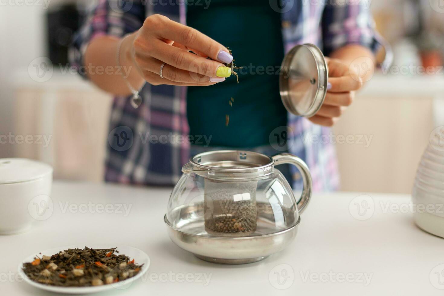 fechar acima do derramando aromático ervas dentro chaleira para faço chá dentro manhã para café da manhã. preparando chá dentro a manhã, dentro uma moderno cozinha sentado perto a mesa. colocando com mãos, saudável ervas dentro Panela. foto