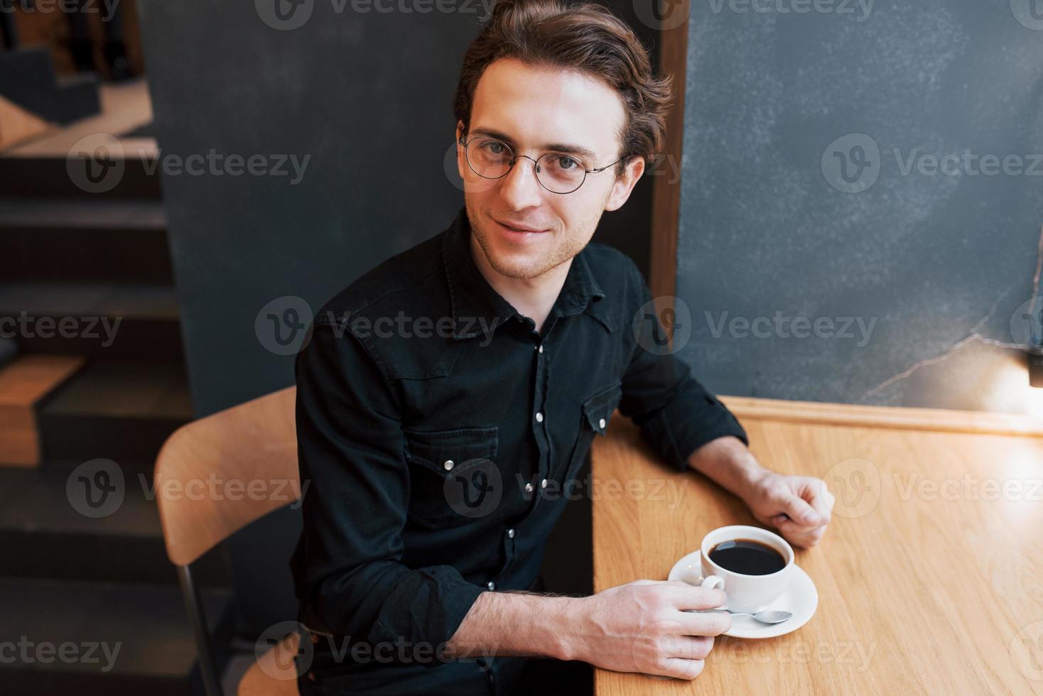 bonito homem barbudo de camisa xadrez segurando um garfo, comendo no café e sorrindo, olhando para a câmera foto