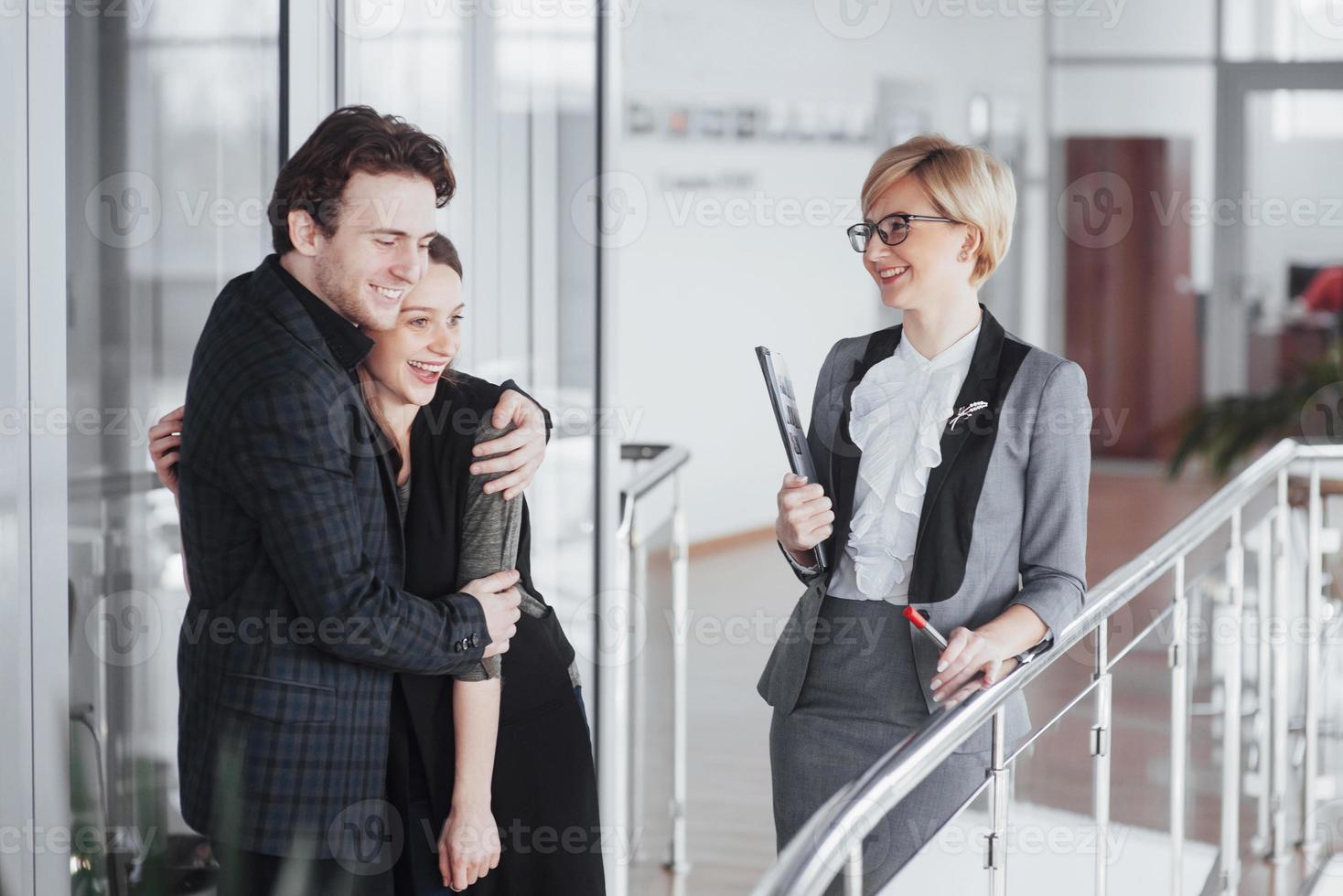 agora seu sonho se torna realidade. dois felizes jovens proprietários atraentes de um carro, elegante vendedor no fundo foto