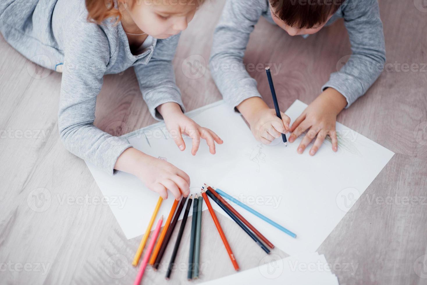 crianças deitam-se no chão de pijama e desenham a lápis. criança fofa pintando a lápis foto