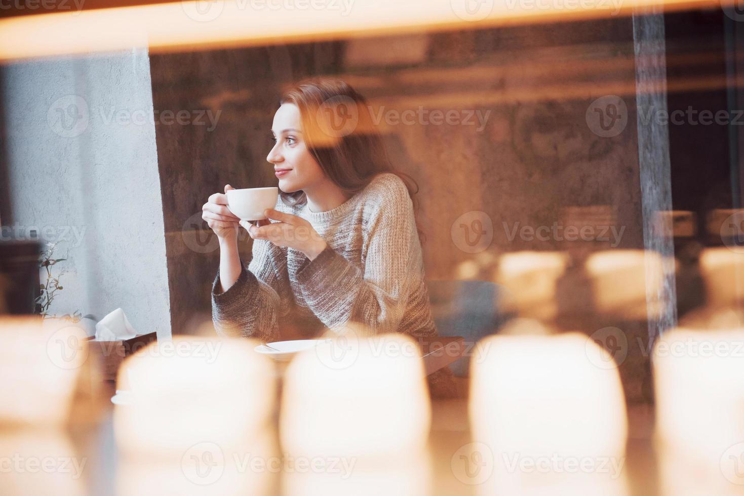 mulher jovem e bonita tomando café cappuccino com espuma perto da janela em um café foto