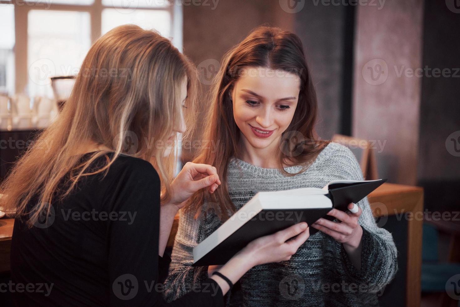 duas garotas absortas na leitura de um livro durante o intervalo no café. lindas mulheres jovens estão lendo um livro e tomando café foto