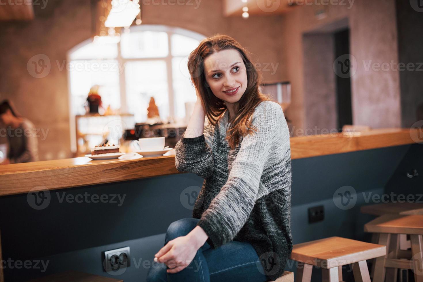 mulher sorridente no café usando telefone celular e mensagens de texto nas redes sociais, sentada sozinha foto