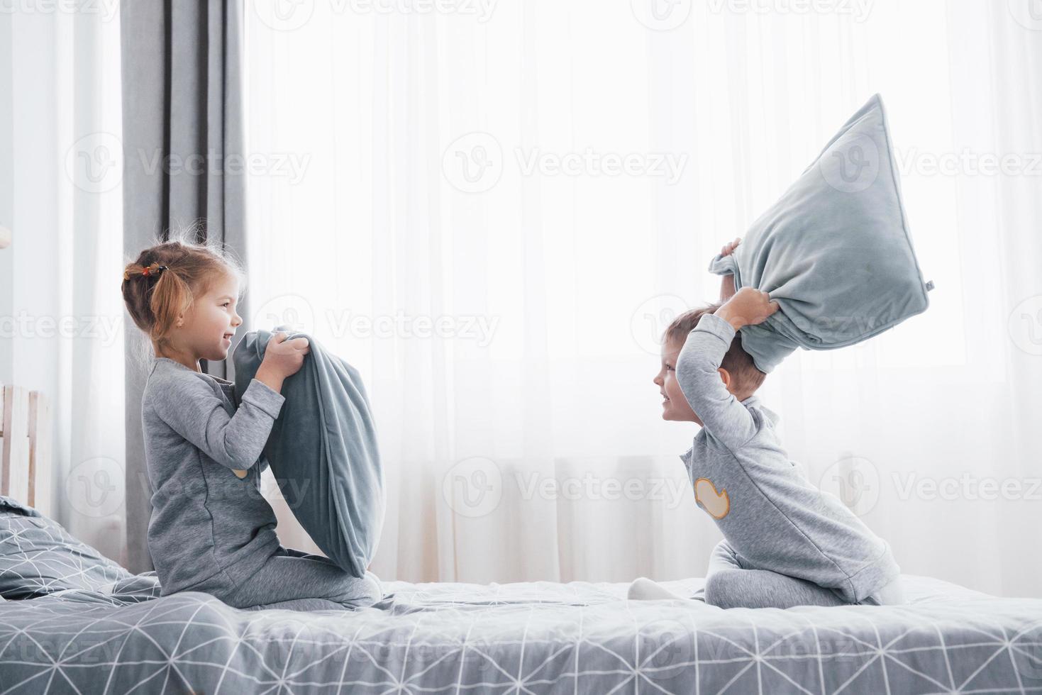 menino e menina encenaram uma luta de travesseiros na cama no quarto. crianças travessas batem umas nas outras nos travesseiros. eles gostam desse tipo de jogo foto