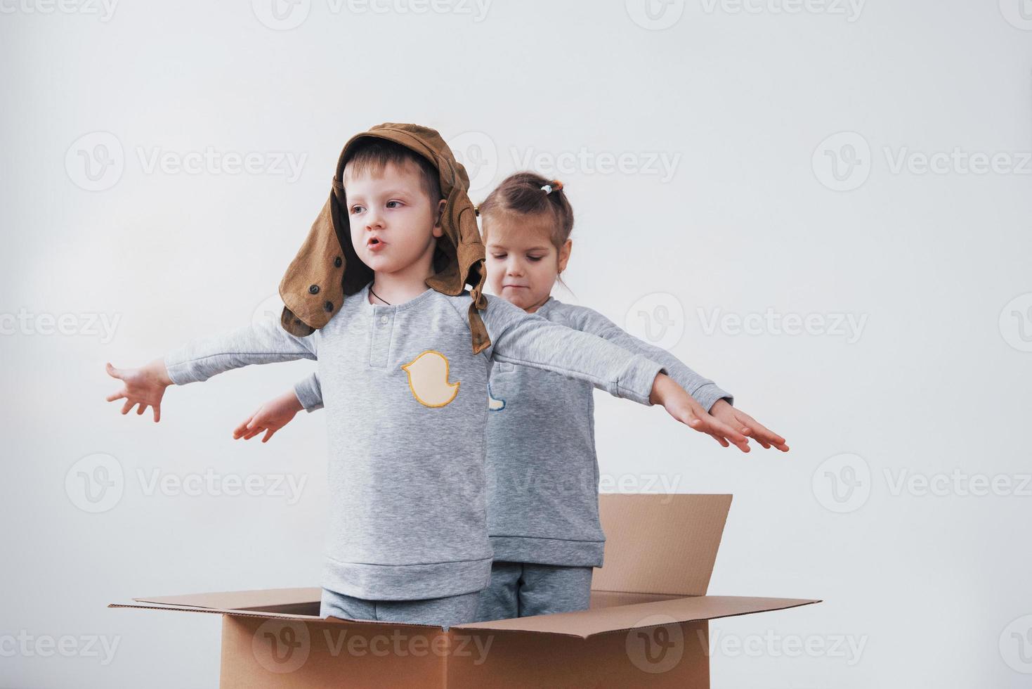 infância lúdica. garotinho se divertindo com a caixa de papelão. menino fingindo ser piloto. menino e menina se divertindo em casa foto