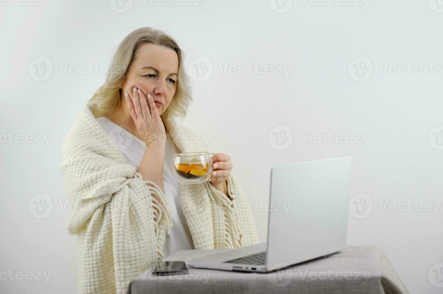 dor de dente mulher segurando dela mão em dela bochecha e olhando às tela monitor segurando chá com limão dentro dela mão coberto com uma cobertor preocupação expectativa notícia Terrível tristeza duvida branco fundo foto