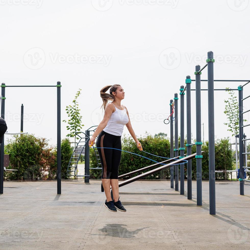 mulher feliz malhando no campo de esportes em um dia ensolarado de verão pulando corda foto