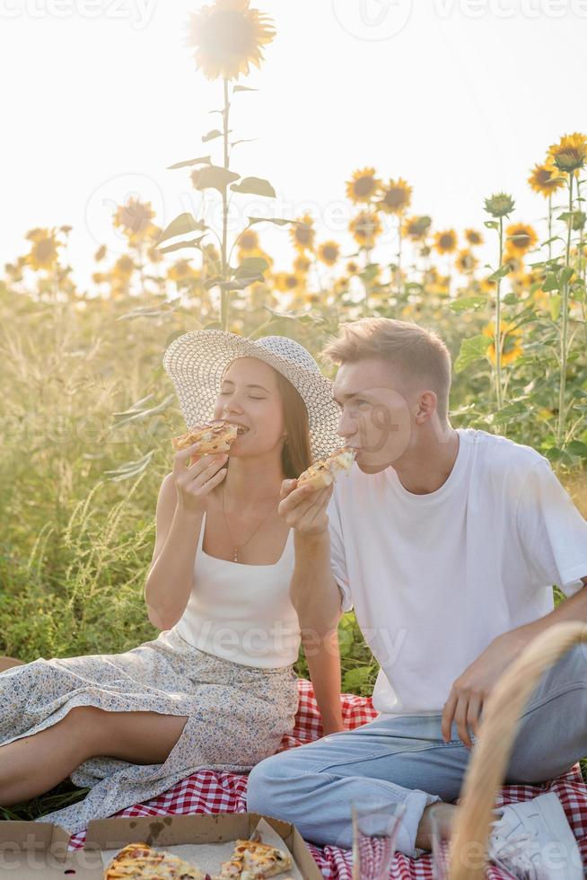 jovem casal fazendo piquenique no campo de girassol ao pôr do sol foto