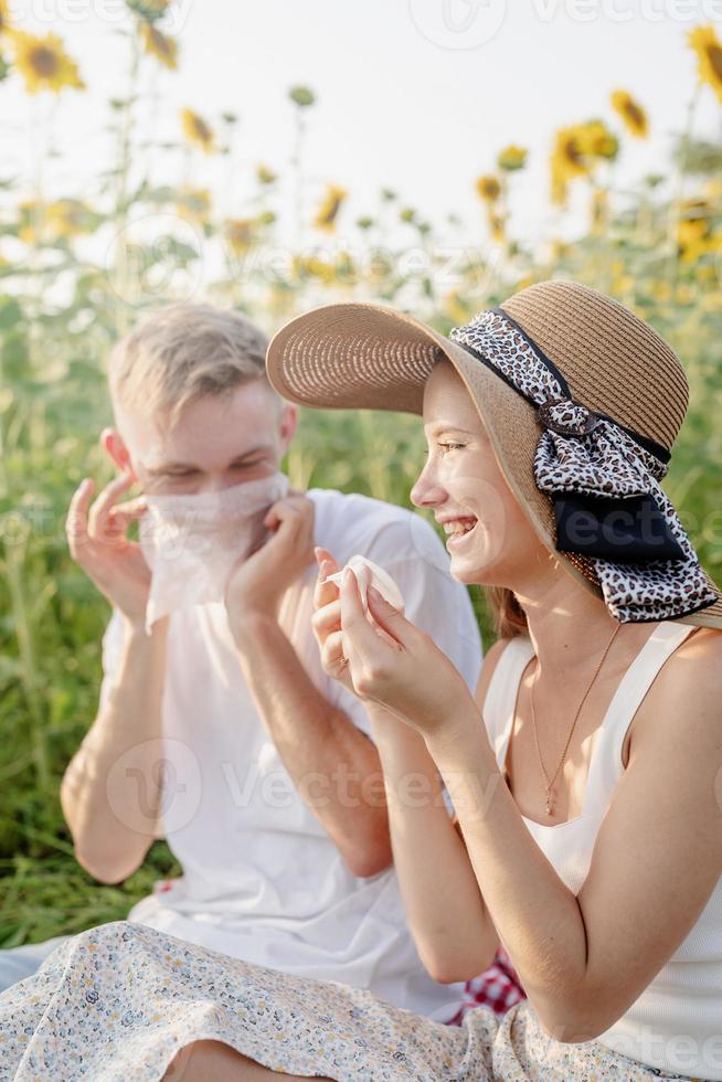 jovem casal fazendo piquenique no campo de girassol ao pôr do sol, limpando as mãos e o rosto foto