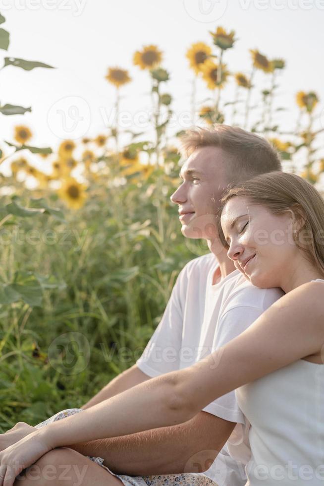 casal jovem fazendo piquenique no campo de girassol ao pôr do sol, mulher deitada no ombro do namorado foto