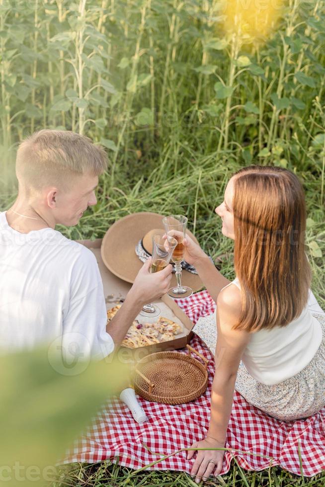 jovem casal fazendo piquenique no campo de girassol ao pôr do sol foto