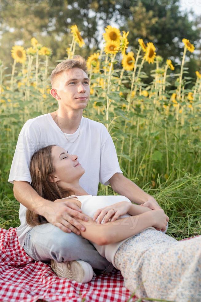 jovem casal fazendo piquenique no campo de girassol ao pôr do sol foto