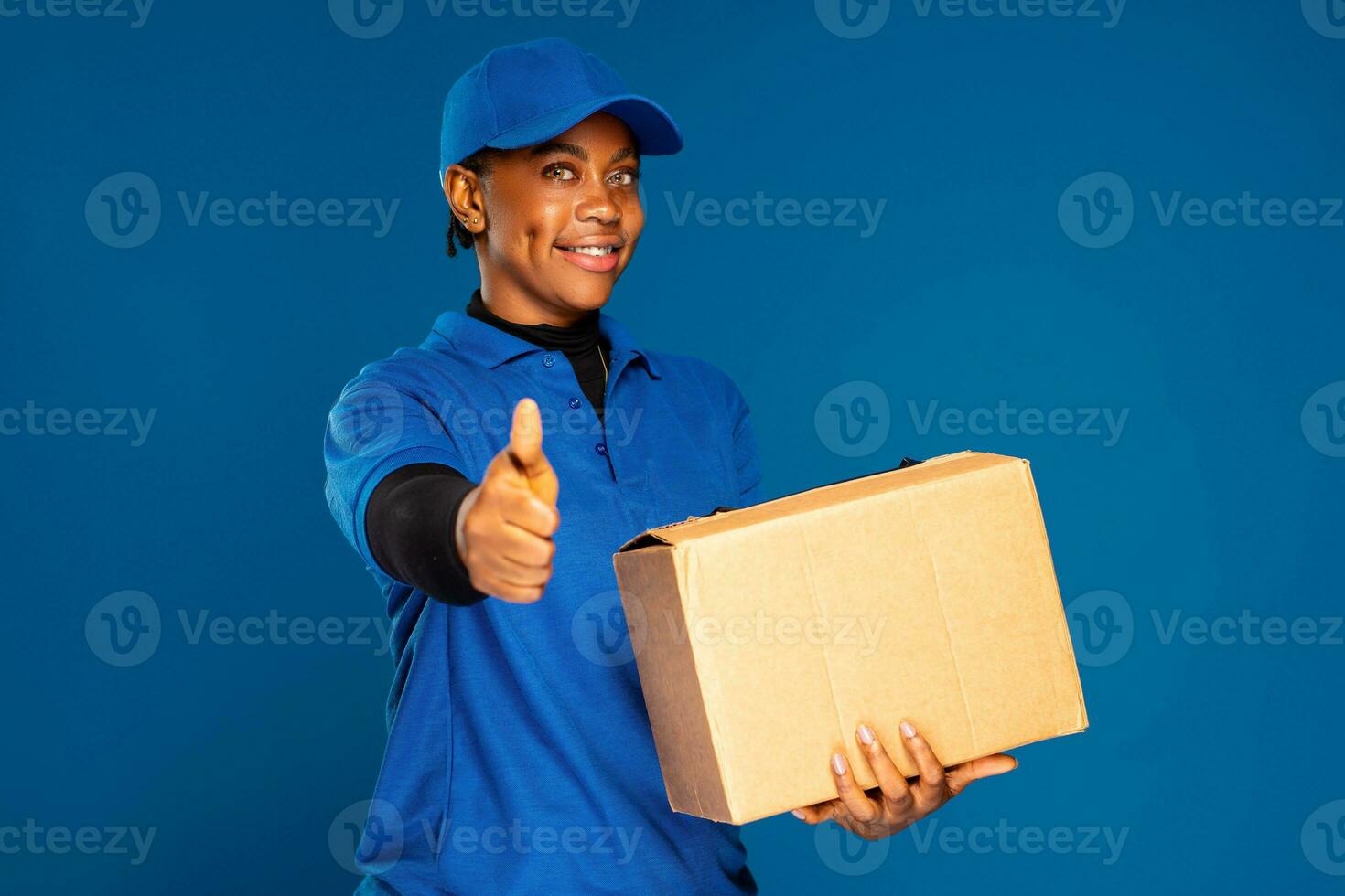 lindo africano fêmea correio trabalhador segurando uma caixa, faz uma polegares acima gesto foto