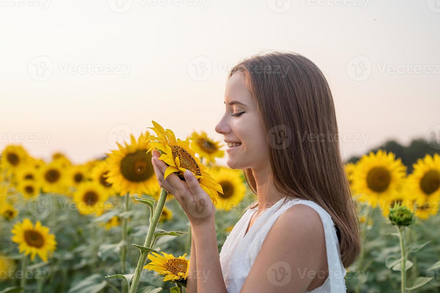 garota de vestido branco cheirando a flor de girassol. foto
