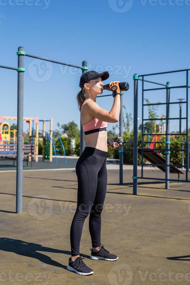 jovem desportiva com luvas desportivas a beber água no campo desportivo foto