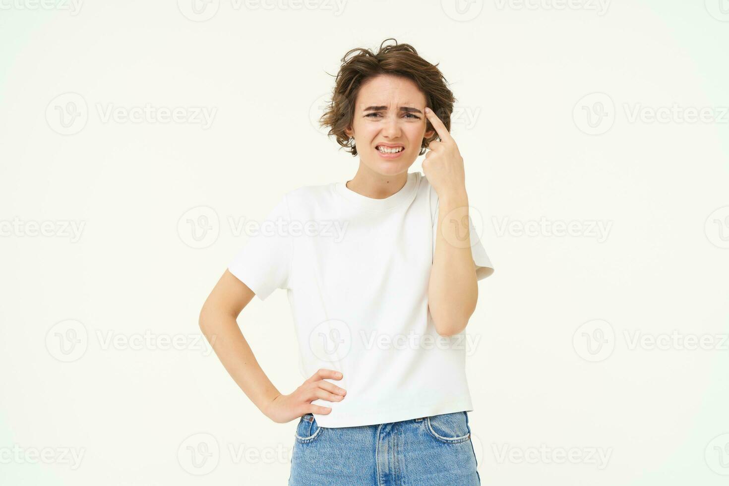 retrato do mulher reagindo para smth ridículo, apontando dedo às testa e carrancudo, reclamando às alguém estúpido, em pé sobre branco fundo foto