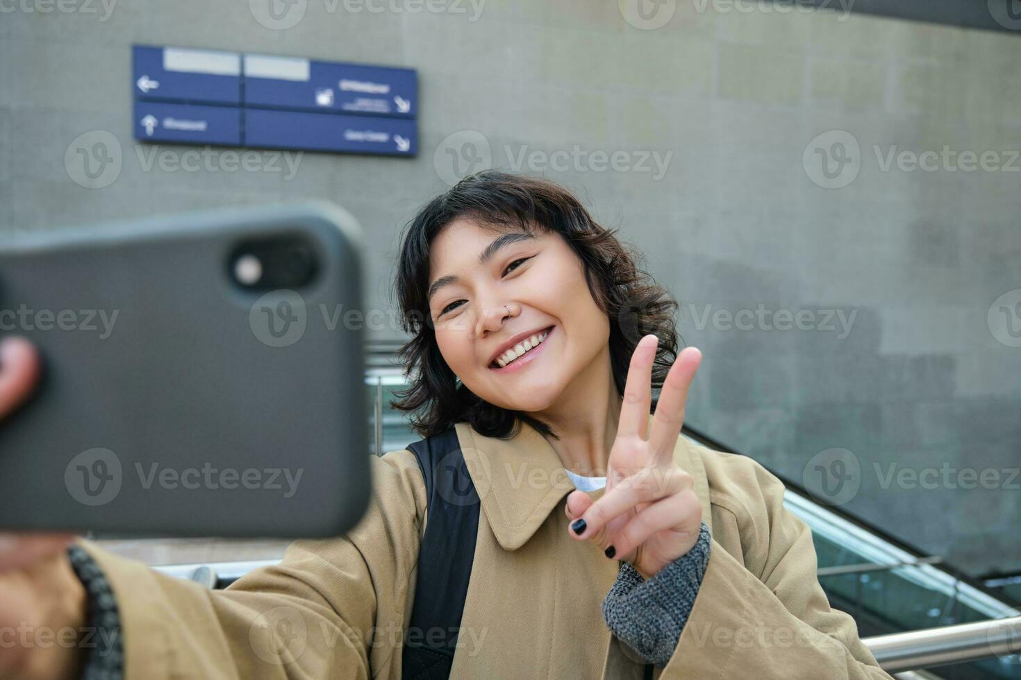 retrato do à moda coreano garota, aluna leva selfie em rua, detém Smartphone e poses em Está Câmera, faz vídeo em turista viagem, sorrisos com alegria foto