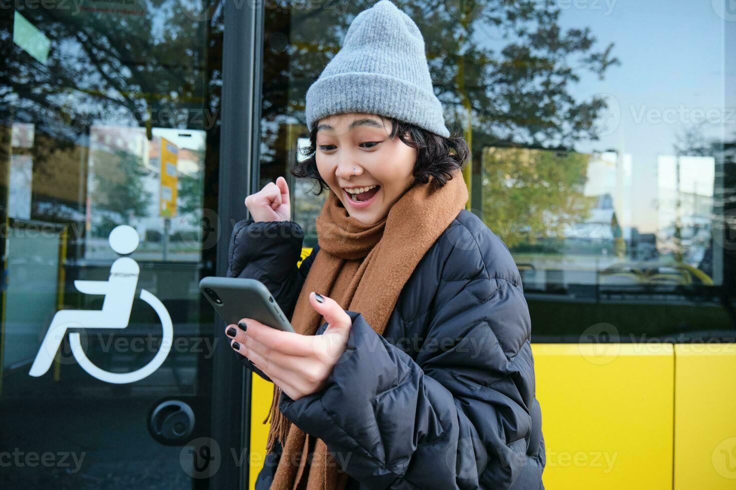 moderno pessoas e estilo de vida. feliz ásia menina gritos a partir de alegria, comemora, carrinhos perto ônibus público transporte e parece espantado foto