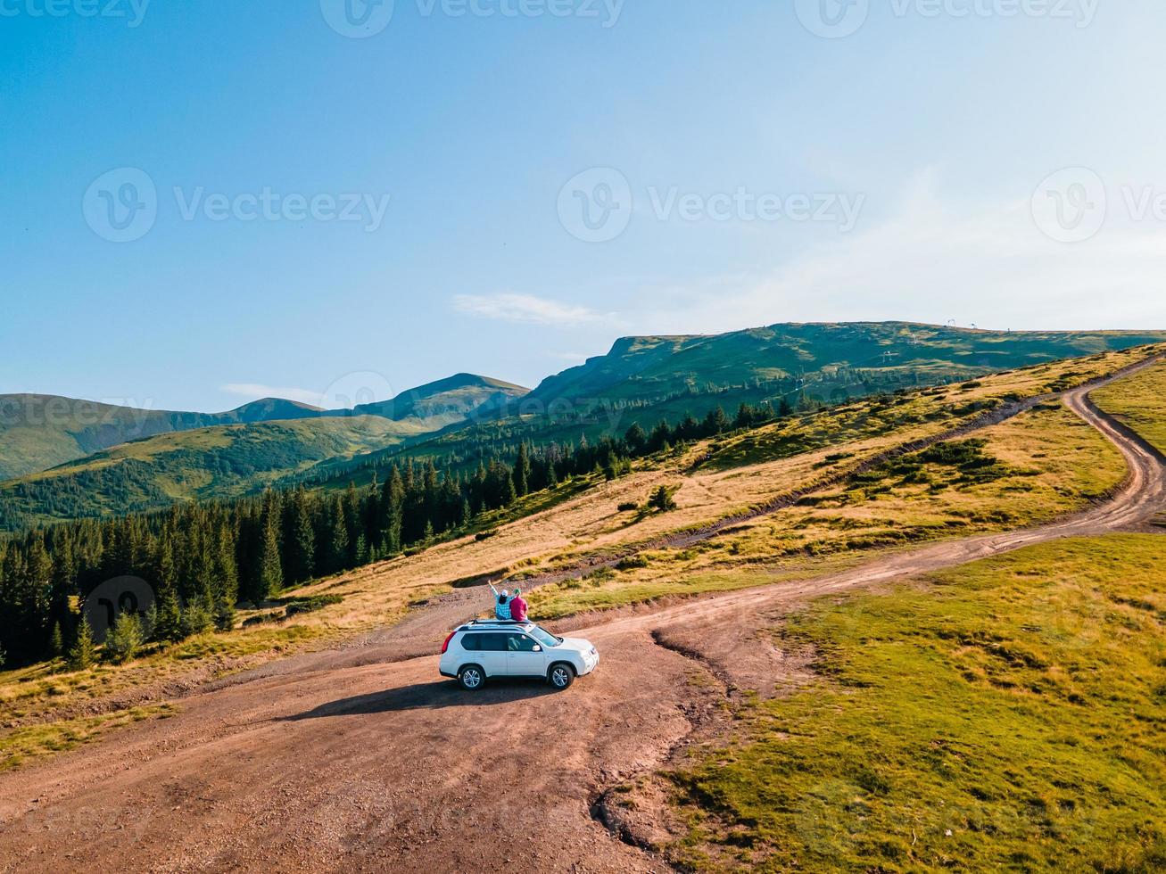 vista aérea de casal sentado no telhado do carro suv apreciando a vista das montanhas foto