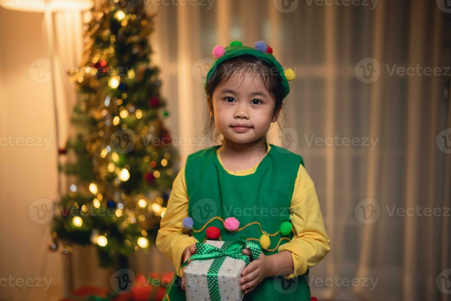 Natal, natal, inverno conceito. ásia bebê criança menina segurando presente caixas sorridente feliz alegre. comemora a feliz Novo ano perto a Natal árvore dentro uma vivo quarto às lar. foto