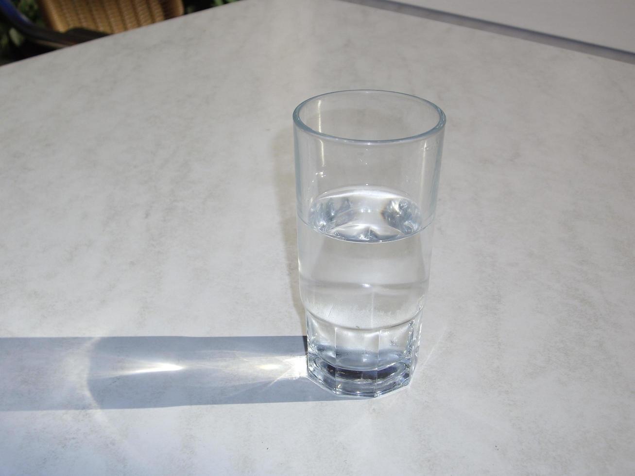 um copo transparente com água fica em uma mesa branca foto
