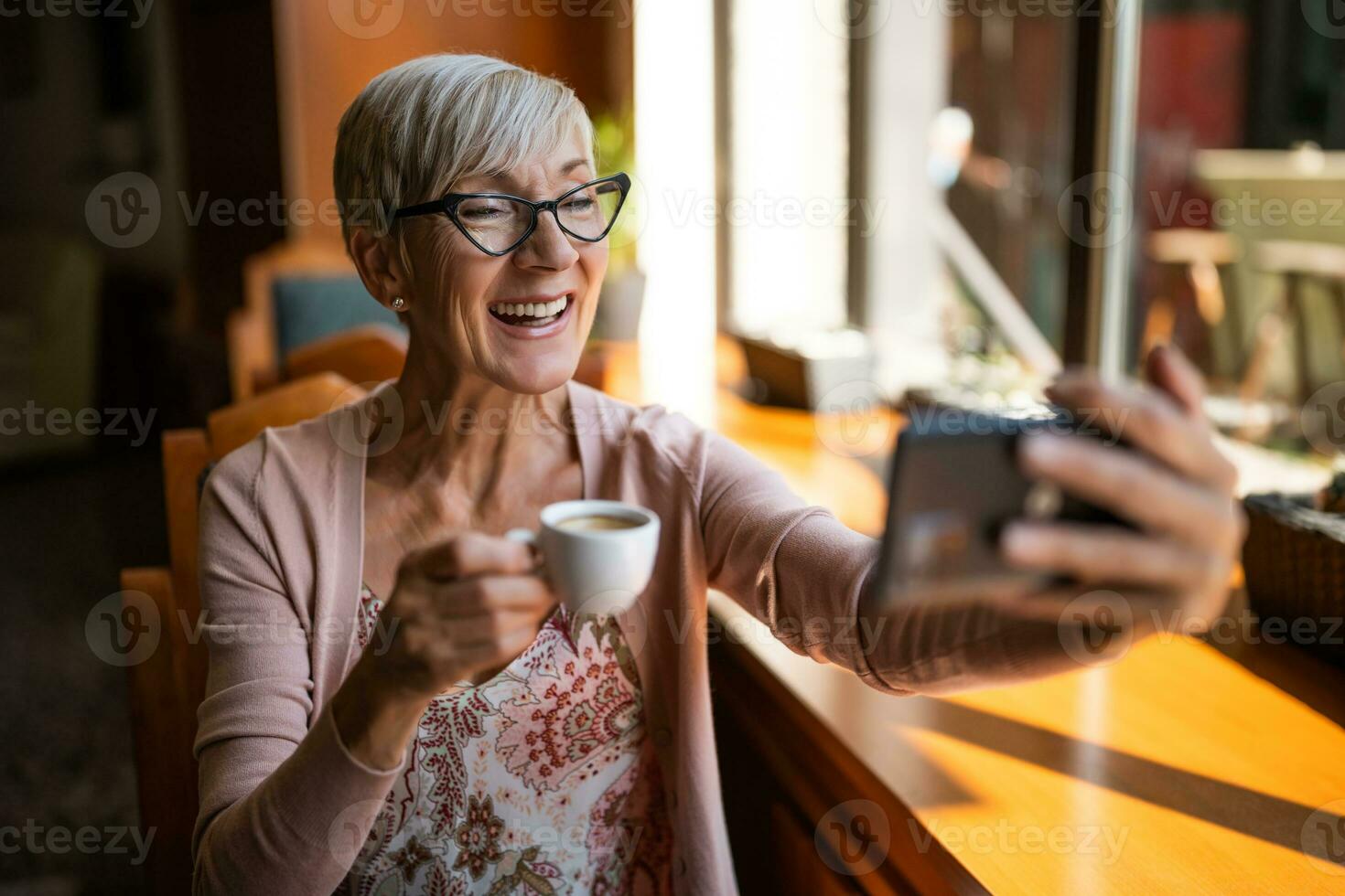 maduro mulher é sentado dentro cafeteria e relaxante. ela é usando Smartphone. foto