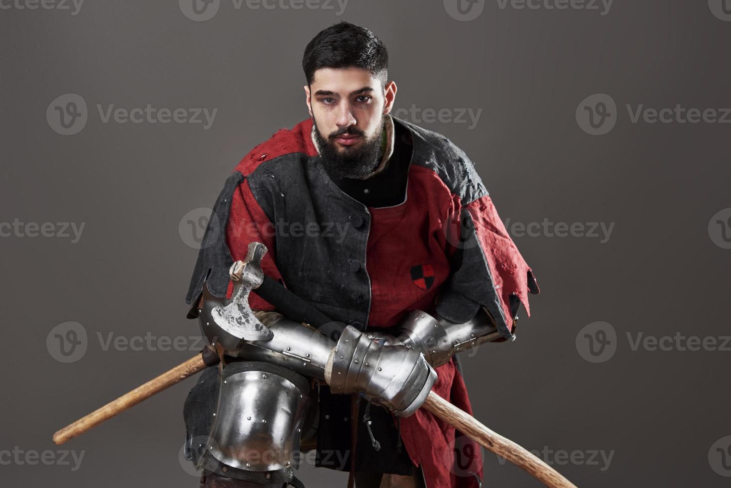 cavaleiro medieval em fundo cinza. retrato de guerreiro brutal com rosto sujo com cota de malha, roupas vermelhas e pretas e machado de batalha foto