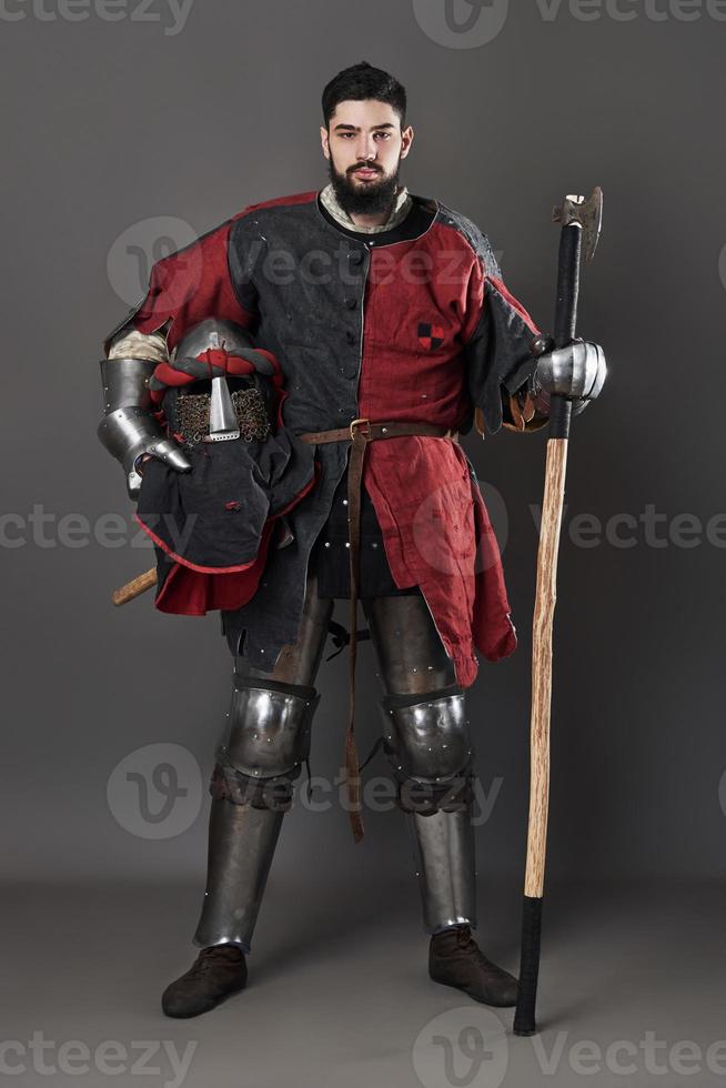 cavaleiro medieval em fundo cinza. retrato de guerreiro brutal com rosto sujo com cota de malha, roupas vermelhas e pretas e machado de batalha foto