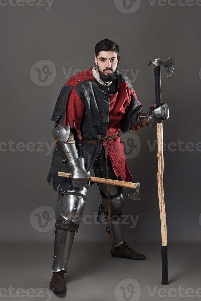 cavaleiro medieval em fundo cinza. retrato de guerreiro brutal com rosto sujo com cota de malha, roupas vermelhas e pretas e machado de batalha foto