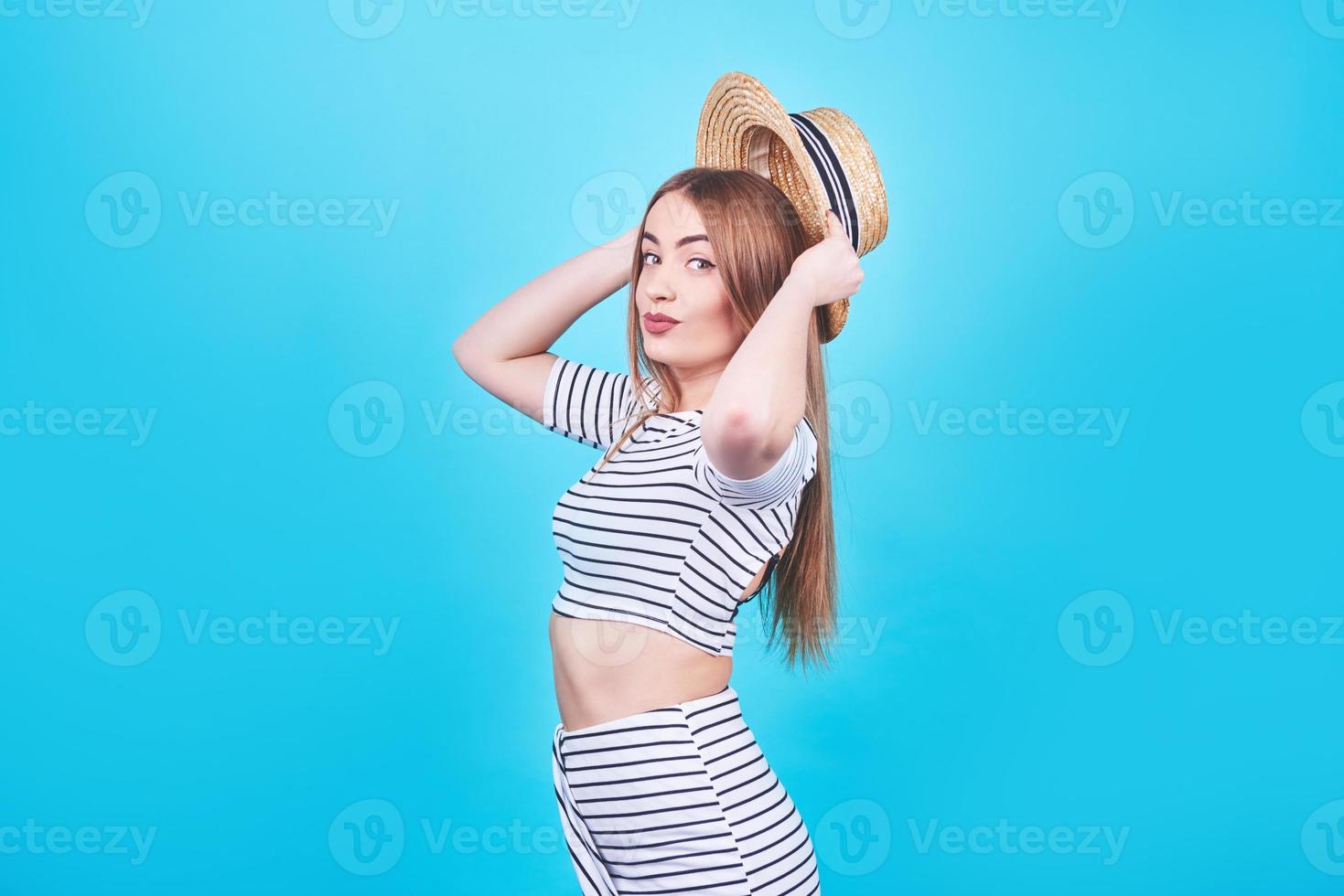 garota atraente em listras brancas e pretas, chapéu, óculos escuros, boca emocionalmente aberta sobre um fundo azul brilhante com um corpo perfeito. isolado. tiro de estúdio foto