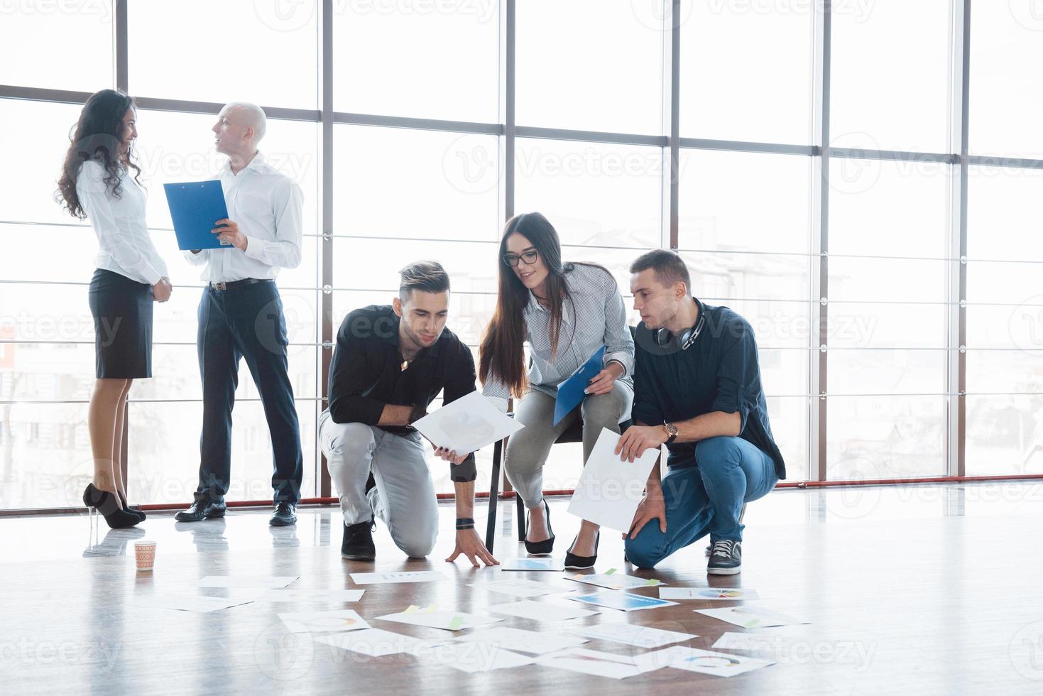 estratégia de planejamento em conjunto. equipe de negócios olhando papéis no chão com o gerente apontando para uma ideia. cooperação realização corporativa. planejamento desenho desenho. conceito de trabalho em equipe foto