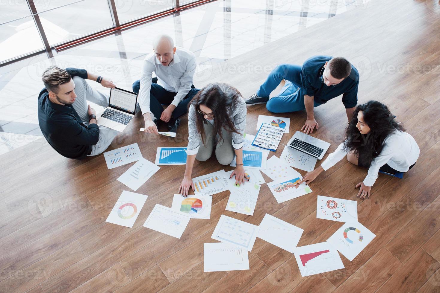 estratégia de planejamento em conjunto. equipe de negócios olhando papéis no chão com o gerente apontando para uma ideia. cooperação realização corporativa. planejamento desenho desenho. conceito de trabalho em equipe foto