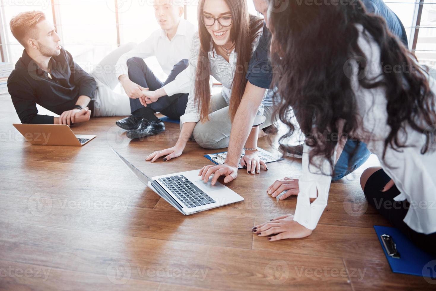 jovens criativos em um escritório moderno. grupo de jovens empresários está trabalhando junto com o laptop. freelancers sentados no chão. cooperação realização corporativa. conceito de trabalho em equipe foto