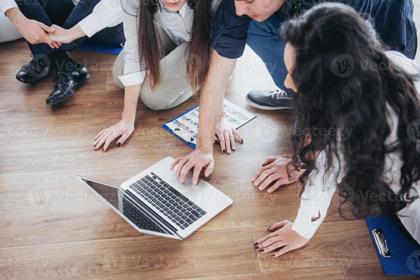 jovens criativos em um escritório moderno. grupo de jovens empresários está trabalhando junto com o laptop. freelancers sentados no chão. cooperação realização corporativa. conceito de trabalho em equipe foto