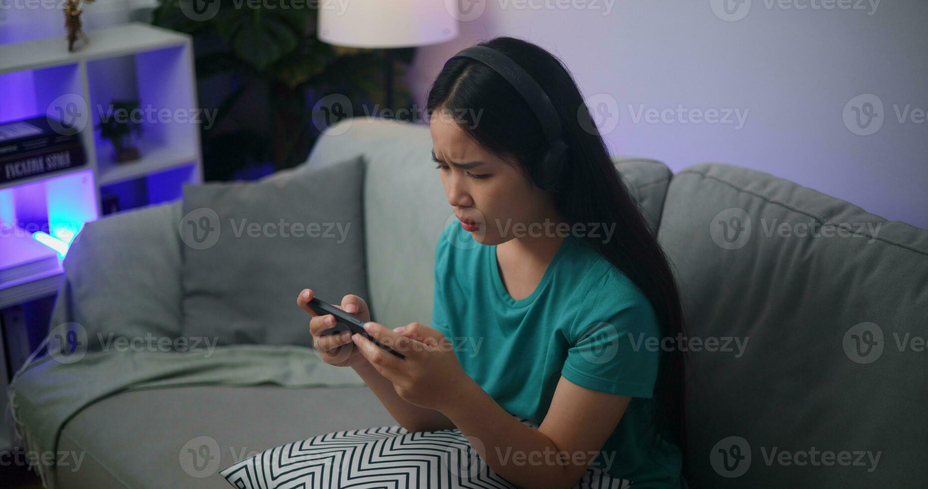 retrato do jovem ásia mulher sério jogando a conectados jogos frustrado com perda ou fracasso sentado em sofá dentro vivo quarto às home.gamer estilo de vida conceito. foto