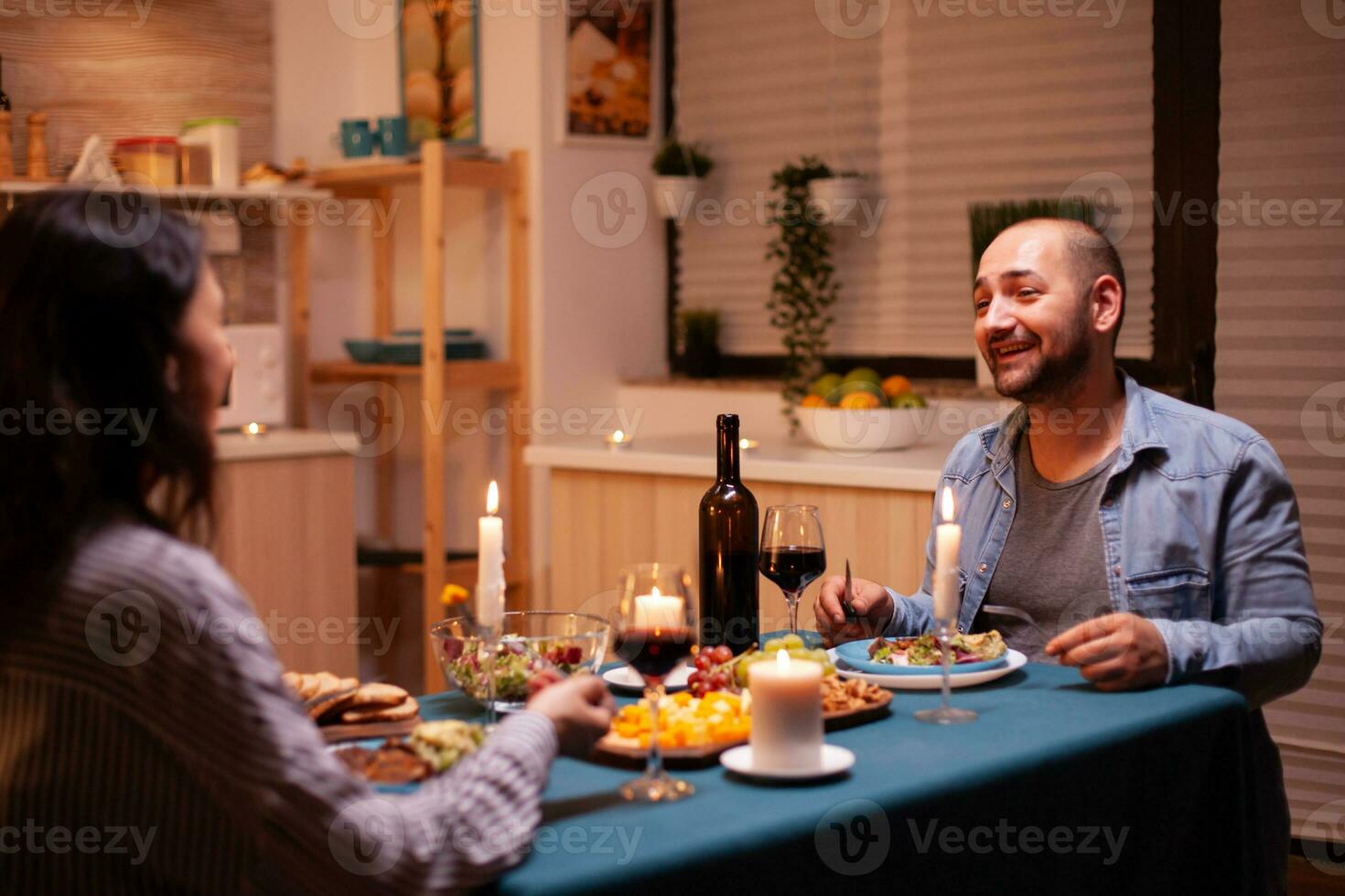 marido dizendo uma história para esposa dentro cozinha durante festivo jantar. relaxar feliz pessoas, sentado às mesa dentro cozinha, desfrutando a refeição, a comemorar aniversário dentro a jantar quarto foto