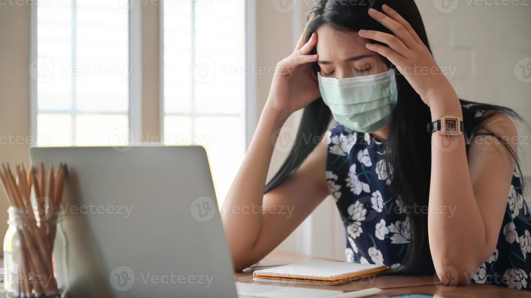 garota usando uma máscara e tocando a cabeça, ela trabalha em casa para se proteger contra o vírus covid-19. foto