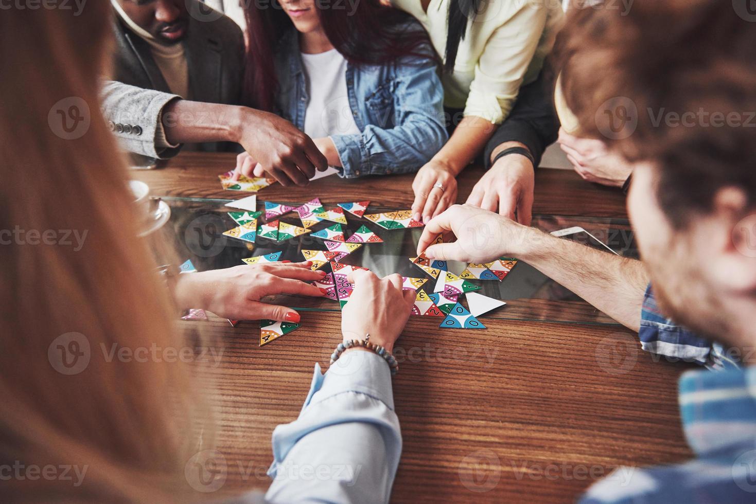 grupo de amigos criativos sentados à mesa de madeira. pessoas se divertindo jogando jogo de tabuleiro foto