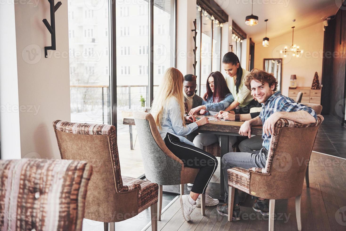 grupo de amigos criativos sentados à mesa de madeira. pessoas se divertindo jogando jogo de tabuleiro foto