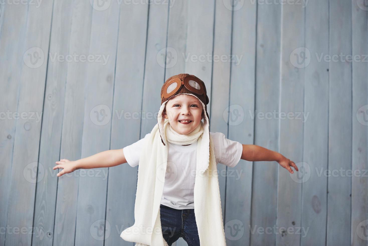 linda criança sorridente no capacete em um fundo azul, brincando com um avião. conceito de piloto vintage foto