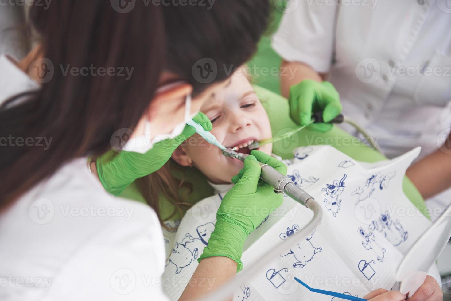 mãos irreconhecíveis de dentista pediatra e assistente, fazendo o procedimento de exame para uma linda garotinha sorridente sentada na cadeira do hospital foto