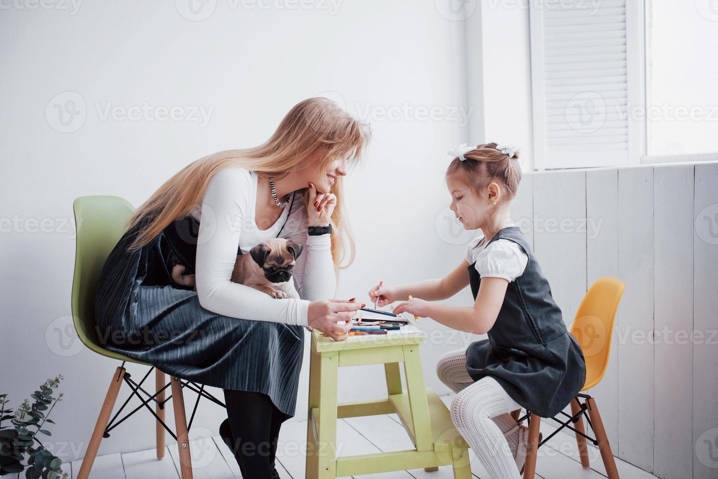 mãe e filho que a filha desenha estão engajados na criatividade no jardim de infância. pequeno pug com eles foto