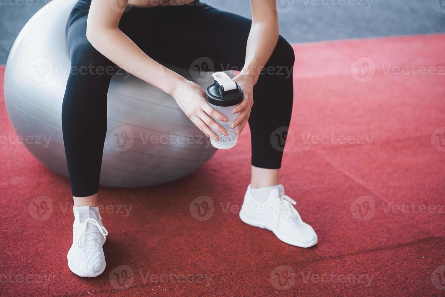 relaxar após o treino. vista de uma bela jovem olhando para longe enquanto está sentado na esteira de exercícios na academia foto