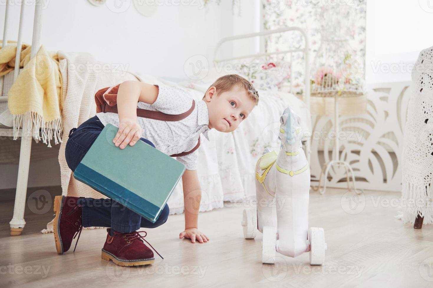 menino bonito vai para a escola pela primeira vez. criança com mochila escolar e livro. criança faz uma pasta, quarto de criança em um fundo. de volta à escola foto